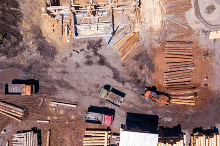 Aerial view of the construction site during the building of a wooden house from thick beams of sawn trees with construction equipment, tractors and trucks. Deforestation and woodworking industry.の写真素材