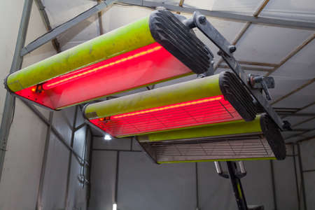 Infrared drying of car body parts after applying putty and paint on a white off-road vehicle in the...