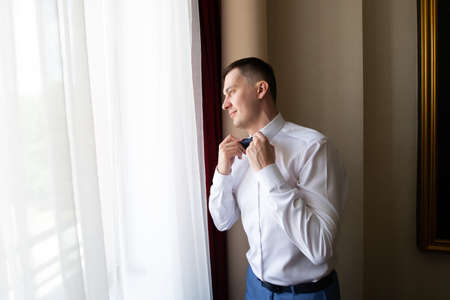 A young man husband is going to a wedding ceremony in a luxury hotel wearing a blue suit and adjusting his bow tie while waiting for the bride. Love and lovestory during the groom's gatherings.の写真素材