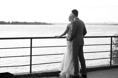 Young beautiful couple of newlyweds with bride and groom walk on the terrace by the ocean during a wedding ceremony in a wedding dress and suit kissing and hugging. Love and lovestory.の写真素材