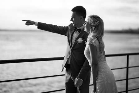 Young beautiful couple of newlyweds with bride and groom walk on the terrace by the ocean during a wedding ceremony in a wedding dress and suit kissing and hugging. Love and lovestory.の写真素材