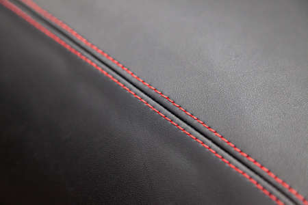 A view of a part of the interior of the car dashboard from leather of black color, stitched double thread of red color with contrast stitching in a vehicle interior design workshopの写真素材