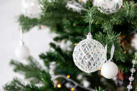 Christmas tree toy decorations of white color balls and garlands on a green coniferous tree before the new year 2020. Background for cards and congratulations.の写真素材