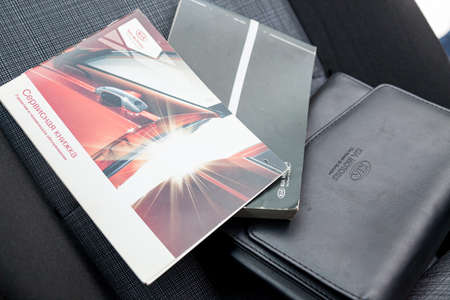 Novosibirsk, Russia - 11.21.2019: Service book of red color, operation manual and black leather cover on the seat of the Kia Motors Russia car.のeditorial素材