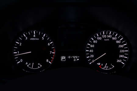 The dashboard of the car is glowing white with arrows at night with a speedometer, tachometer and...