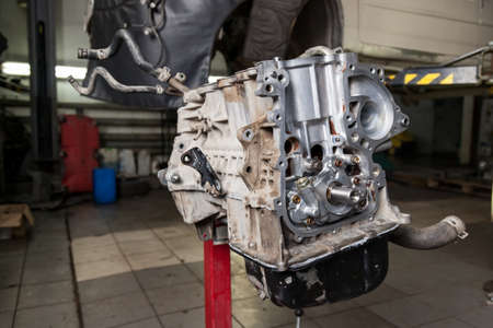 A car raised on a rotary lift for overhaul repair and under it a detached bottom engine part...