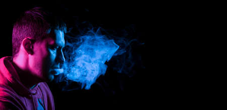 Close up portrait of the face of an adult serious man exhales blue toxic smoke while smoking...