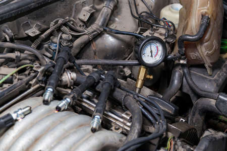 A male mechanic measures the compression in the cylinder of a car engine using a barometer with a scale and an arrow during diagnosis and repair in a workshop for vehicles. Auto service industry.の写真素材
