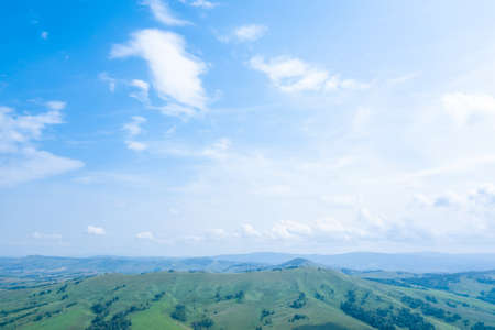 Landscape of green valley flooded with light with lush green grass, a fresh summer day under a blue sky with white cloudsの写真素材