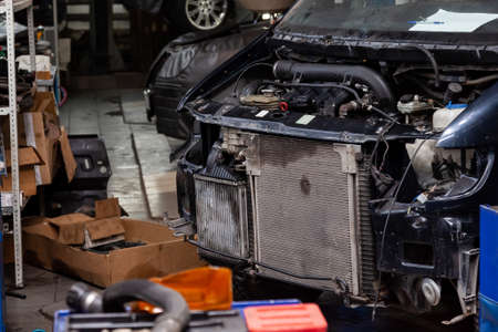 Disassembled black car in the workshop prepared for repair: front end, hood and bumper removed, internal equipment, parts and spare parts visible. Auto service industry.の写真素材
