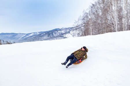 Altai, Russia - 01.01.2020: A man is having fun and riding from the mountain in the snow on an...