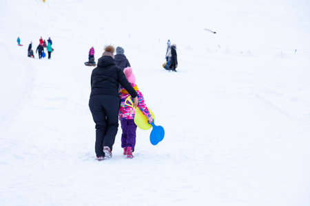 A woman with daughter are having fun and riding from the mountain in the snow on an inflatable round...