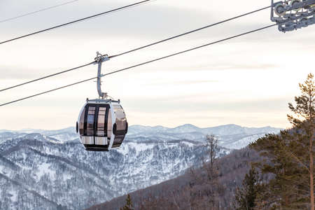 Cabin of a gondola cableway suspended on a rope where sits people with skis and snowboards high in the Altai mountains with snow and blue sky on winter sunset. Ski resorts and snowboarding.の写真素材