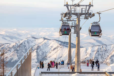 Altai, Russia - 01.01.2020: A gondola cableway with a two booths suspended on a cable with people on the observation deck and snow on winter. Manzherok Ski resorts and snowboarding in Altai mountains.の写真素材