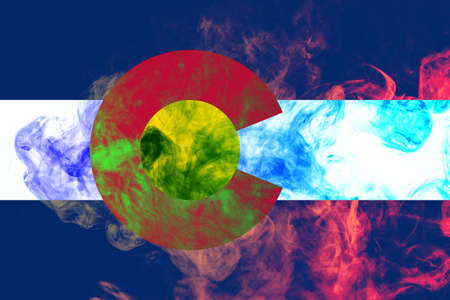 The national flag of the US state Colorado in against a gray smoke on the day of independence in different colors of blue red and yellow. Political and religious disputes, customs and delivery.の写真素材