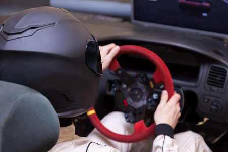 A professional racer in a black helmet and a white homologated suit sits in the sports seat of a car for drifting and racing during a race and training on a simulator.の写真素材