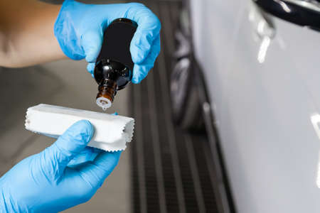 Applying and dripping a drop of nano-ceramic coating on the sponge by a male worker with a chemical...