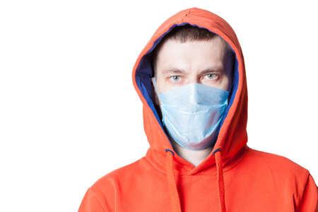 A man in an orange hoodie with a head-clad hood with a medical mask on his face during a coronavirus...