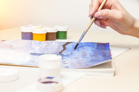 A female hand holds a brush and leads it in a watercolor drawing of blue shades close-up on the...