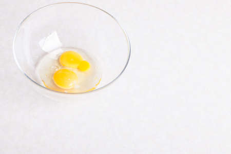 Two broken eggs in a glass transparent bowl on a white table close-up isolated for making an omelet or the main ingredient for baking desserts or dough.の写真素材