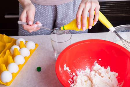 Female hands hold spoon and bottles of ready-made lemon juice in and pour it into the kneading dough...
