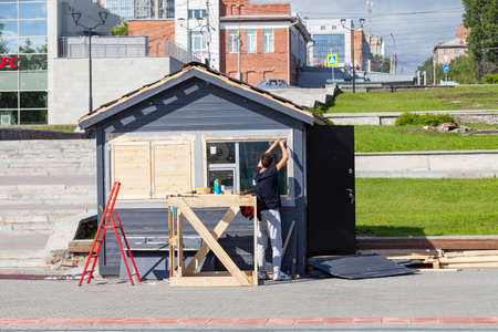 Novosibirsk, Russia - 06.06.2020: A man installs windows in a small village - a kiosk in the park preparing a stall for seasonal sale of goods in a park in the city center: food, drinks, ice creamのeditorial素材