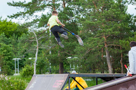 Novosibirsk, Russia - 06.06.2020: A company of teenagers spends time in the park riding a bicycle and scooters. A teenager boy will perform a trick by bouncing up on a ramp.のeditorial素材