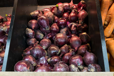 Red onions in a tray on a counter in a self-service supermarket. Fruit is a source of useful elements and vitamins. A healthy product in the daily diet of vegetarians and people.の写真素材