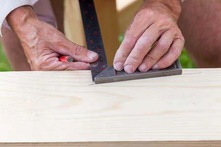 Close-up of the hands of an elderly craftsman - carpenter at work holding a metal ruler and a...