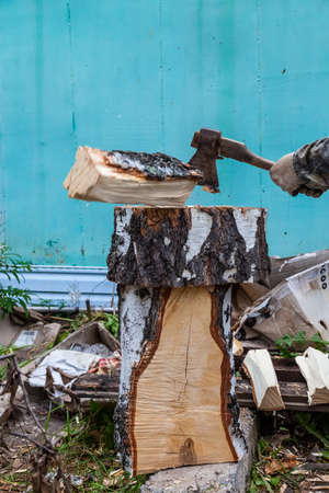 A log flying off to the side from a deck when an ax is struck in men's hands in cloth gloves against...