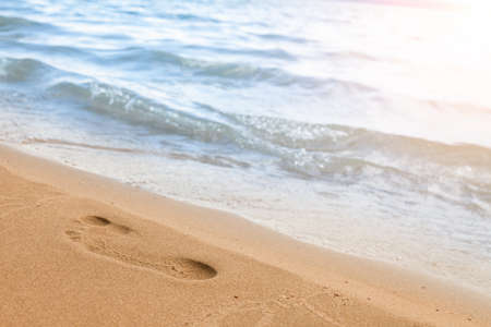 Close-up of the beach shore with a man's footprint on the yellow sand along the line of the blue sea...