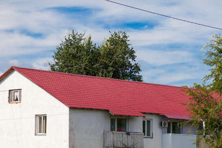 The roof of an old wooden house covered with sheets of brown metal tiles on a background of green coniferous trees on a summer day. Business selling building materials or helping low-income families.の写真素材