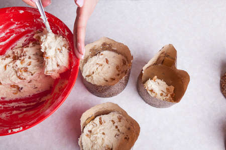 Close-up of a workplace with brown paper baking dishes and the hands of a chef who spoon picks up...