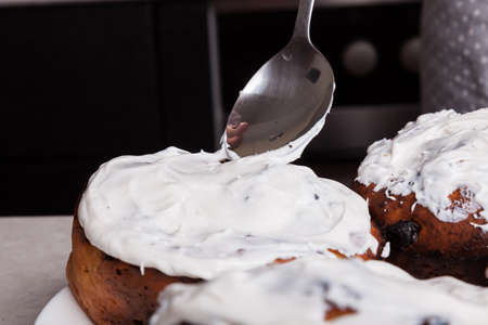 Close-up - decorating homemade Easter cakes with white icing - a mixture of beaten eggs and sugar with a metal spoon. Self-isolation hobby.の写真素材