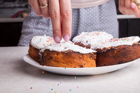 Close-up of freshly baked Easter cakes on a plate and female hands with manicure decorating with...