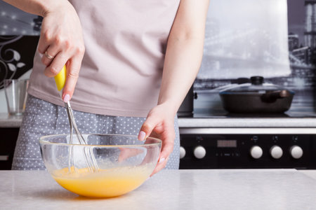 A woman in the kitchen holds a whisk in her hands with a yellow handle and whips them with eggs in a...