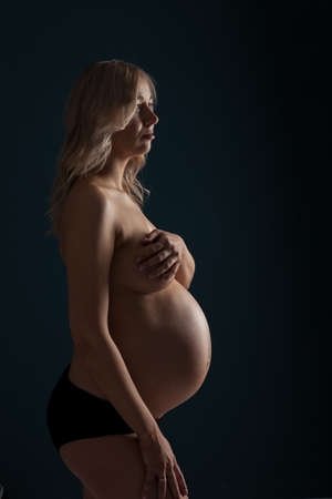 Silhouettes of a pregnant beautiful woman naked topless and covering her breast with a big belly in anticipation of the birth of a child.の写真素材