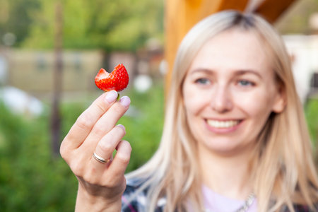 A ripe strawberry from which a young woman has bitten off. The focus is on the strawberry in foreground.の写真素材