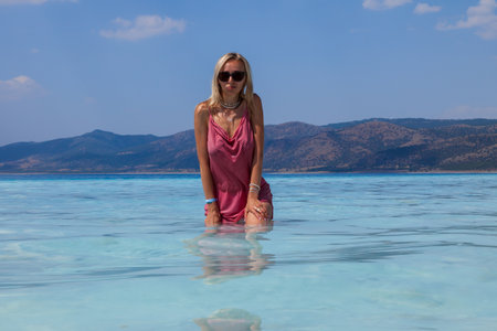Young caucasian woman in the sunglasses and pink dress sexy posing in the Lake Salda, Turkey. Beautiful female happy relax walking on beach near sea with white sand and very clean blue water.の写真素材