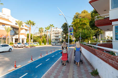 Kemer, Turkey - 08.28.2021: Two Caucasian moms with strollers and kids walking together in Kemer city Turkey. Friends talking on street keeping social distance. A new normal.のeditorial素材