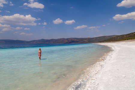 Young caucasian woman in the sunglasses and pink dress standing sexy posing in the Lake Salda, Turkey. Beautiful female happy relax walking on beach near sea with white sand and very clean blue water.の写真素材