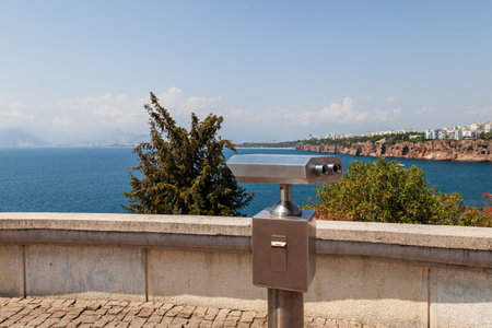 Metal gray coin operated telescope isolated at beautiful summer panoramic view at cityscape, blue sky and sea water. Turkey, Antalya city.の写真素材