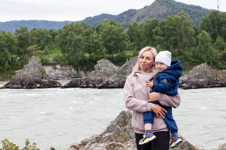 Mother and baby walking on nature outdoors. Family in rocky nature background with river. Loving woman with child in countryside. Concept of green parenting, natural motherhood, postpartum period.の写真素材