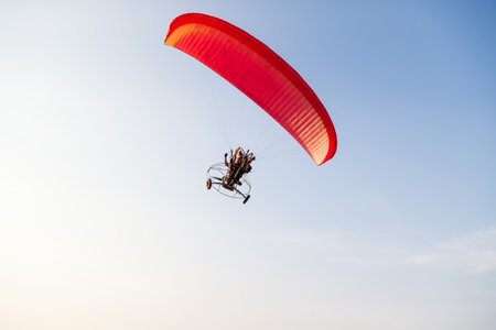a red motorized paraglider in the blue sky flies with two passengers on a warm summer day. Flying sports.の写真素材