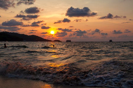 Incredibly picturesque landscape with a view of the waves in the ocean and the bronze sun at the golden hour at sunset in thailand on the island of phuket, patong beachの写真素材