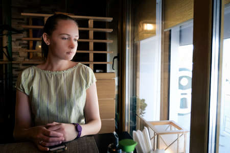 Woman sits in a cafe near the window at the table and waitingの写真素材