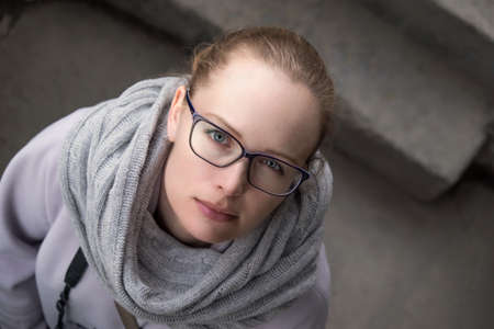 Girl with glasses and with a camera standing in a coat on the street is looking at the cameraの写真素材