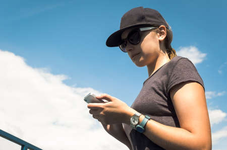 The girl in sunglasses and a baseball cap looking at phoneの写真素材