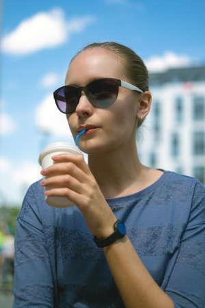 Girl in sunglasses drinking coffee from a paper cup on a sunny summer dayの写真素材