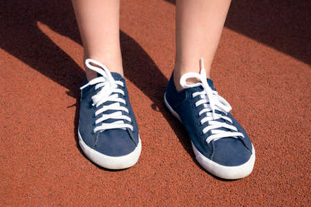 Female feet in blue sneakers on red coating on a sunny dayの写真素材